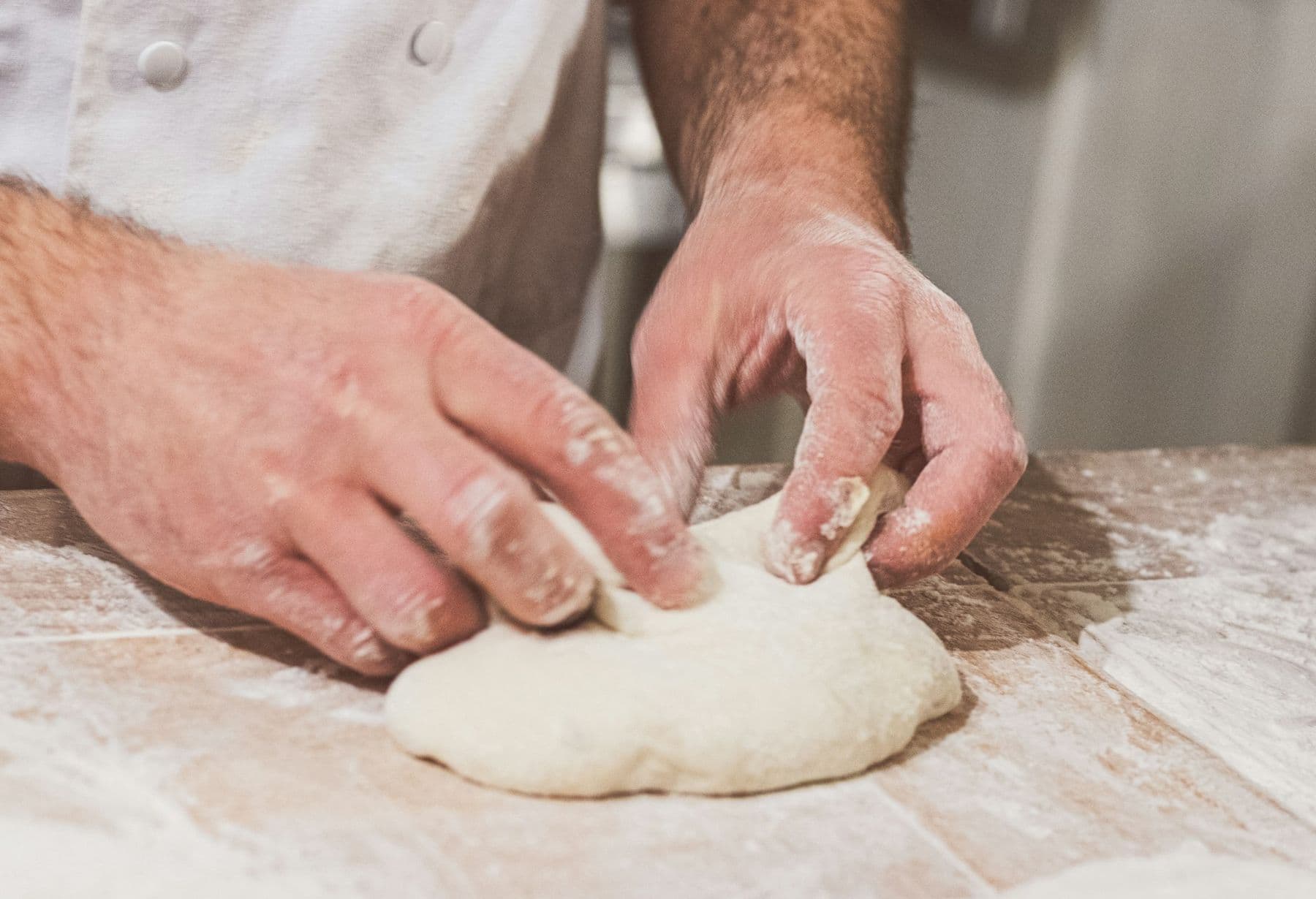 Floured hands kneading dough on a wooden bench