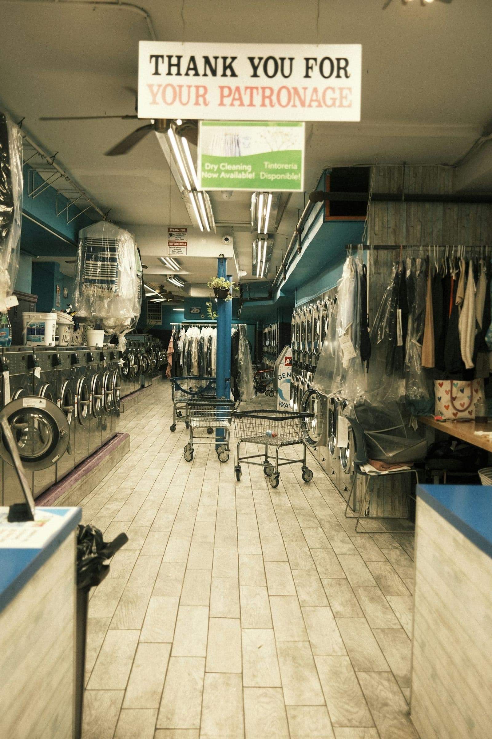 The aisle of a neighborhood laundromat and dry cleaner under a ‘Thank you for your patronage’ sign